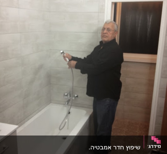 אדם מחזיק צינור מקלחת בחדר אמבטיה משופץ
